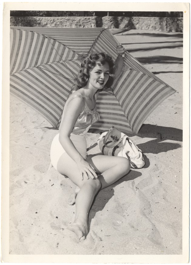 Suzanne Crawford laying in the sand under an umbrella with a bag - 