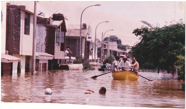 Flooded street scenes and temporary shelters in Ica, Peru - Photograph, recto: [Men rowing a boat in a flooded Ica street, text on the back reads "Flooding, waters reached different levels beacuse of the 'El Niño' phenomenon"]