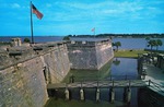 A large postcard showing the walking bridge, moat, and entrance to the Castillo de San Marcos as well as a view out over Matanzas Bay to the inlet, looking East. ca. 1965