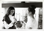 [Artifacts on display in the Pan American Center Museum with docents Janet Poole and Jean Babich, holding ceramic vessel]