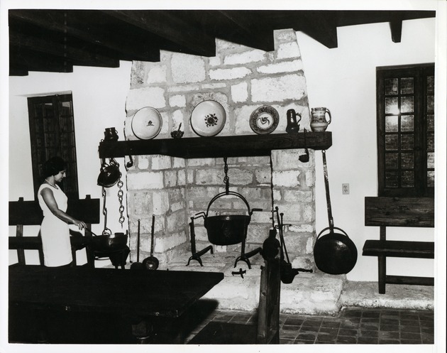[Casa del Hidalgo interior, showing fireplace and associated artifacts with hostess Maria Hugas Acebal] - 