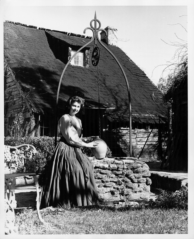 Woman in period dress sitting at a well behind the Oldest School House, looking Southeast