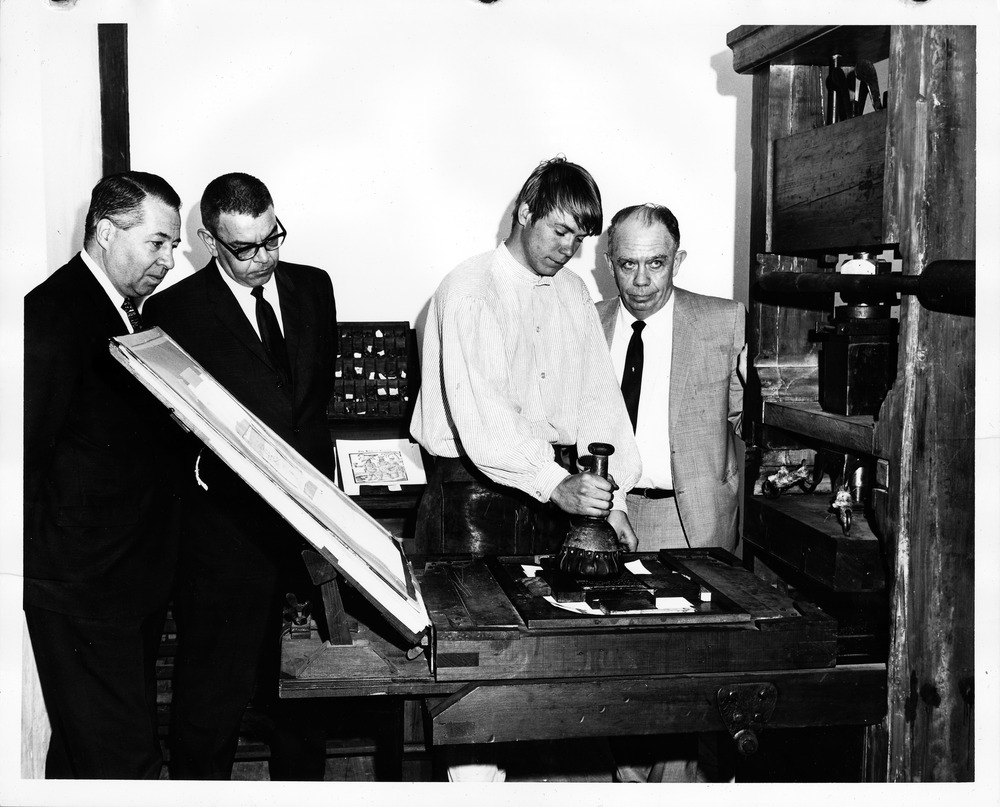 Dennis White giving a demonstration of the replica printing press to Frazier Poole, August Domer, and Francis J. Dobbs during a tour of the restoration area, 1968 - 