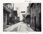 Historic view of St. George Street with several business signs overhanging the street and the Arrivas House with balcony on the left with sign reading "BICYCLES TO HIRE", view from intersection of St. George Street and Cuna Street, looking North