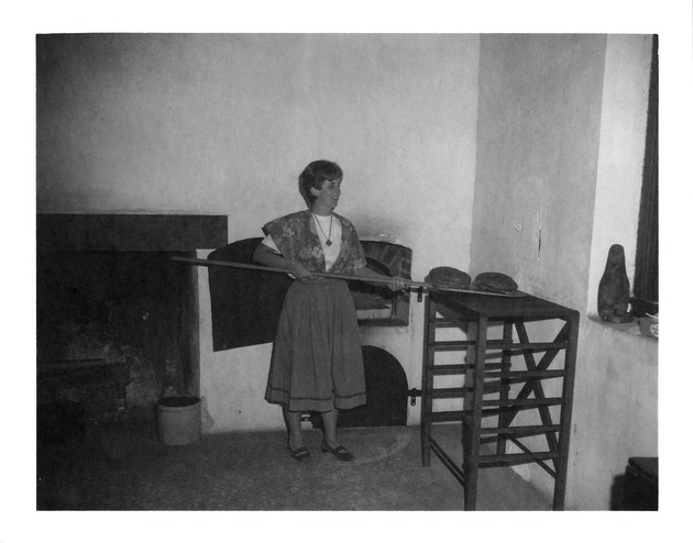 Fireplace and oven in Salcedo Kitchen, Mrs. Busby taking bread out of the oven, 1970