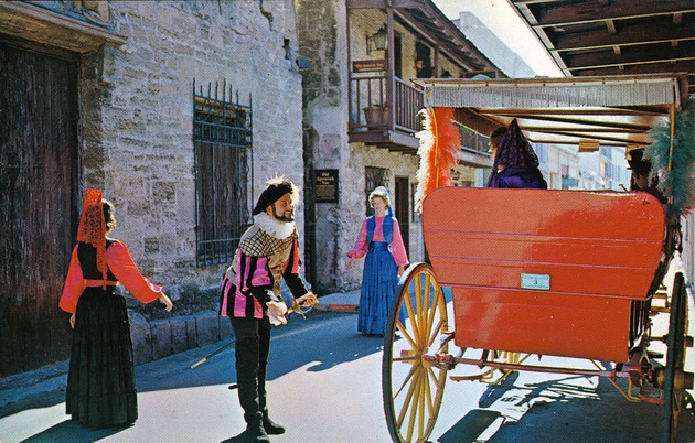 A man in Spanish costume greets woman in a carriage on St. George Street, in front of the Avero House with the De Mesa Sanchez House visible in the background, looking Southeast - 