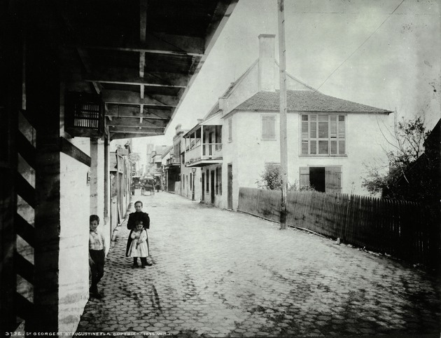 Several children standing in St. George Street near the intersection with Cuna Street (identified by lampost behind the children) with Benet House on right, looking North with the tower of the San Salvador Hotel in the distance on right side of the street