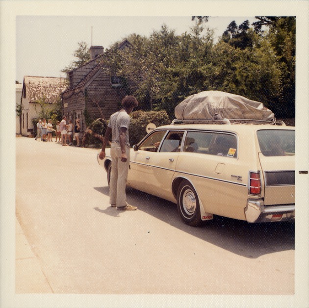 Man standing in the street talking with driver of a car on St. George Street, facing the Oldest Wooden School House (Genopoly House), looking Southwest