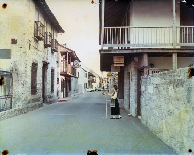 Views of San Agustin Antiguo from St. George Street, ca. 1970 - Woman in period dress in front of the Arrivas House, Avero House and De Mesa Sanchez House on the left, looking South