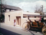 A Woman standing in front the Gallegos House on St. George Street takign a photograph next to a horse-drawn carriage, looking Northeast, ca. 1963