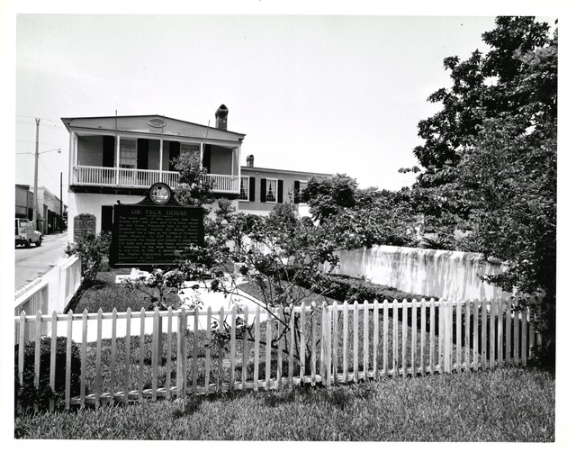 Small garden to the South of the Peña-Peck House with the house beyond and a sign for the "Dr. Peck House" in the yard, looking North, ca. 1965