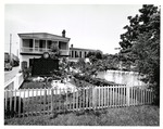 [1965] Small garden to the South of the Peña-Peck House with the house beyond and a sign for the Dr. Peck House in the yard, looking North, ca. 1965