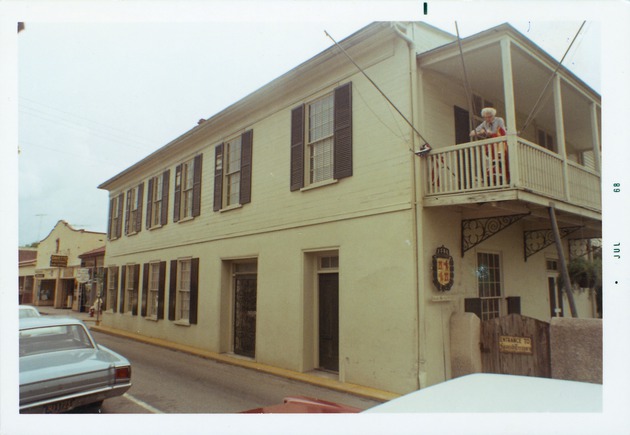 West façade of the Peña-Peck House with a woman hanging flags on the South balcony from St. George Street, looking Northeast, 1968