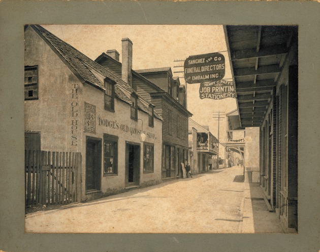 Historic View of the Parades Dodge House as Dodge's Old Qriosity Shop with man standing next to a newspaper rack in front of the Rodriguez-Avero-Sanchez House next-door, looking Northwest