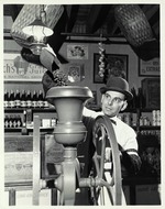 [1965] Man in period dress pours whole coffee beans into a hand-cranked grinder in the Old Store Museum, ca. 1965