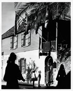 A Woman greets children at the entrance of the Oldest House  with the silhouettes of women in historic Spanish dress in the foreground from St. Francis Street, looking Northwest, 1965