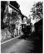 A horse-drawn carriage riding down Aviles Street with the Don Toledo House on the left and the O'Reilly House behind it, looking North, ca. 1965