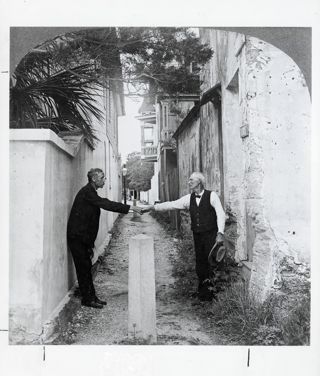 Two men shake hands across narrow Treasury Street from Avenida Menendez (Bay Street), looking West, ca. 1900