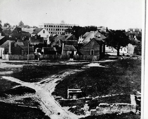 The skyline of St. Augustine and the intersection of Avenida Menendez (Bay Street) and Charlotte Street seen from the grounds of the Castillo de San Marcos, with scaffolding erected on the roof of the Florida House hotel (center) during the construction of an addition to the hotel, looking South, ca. 1875