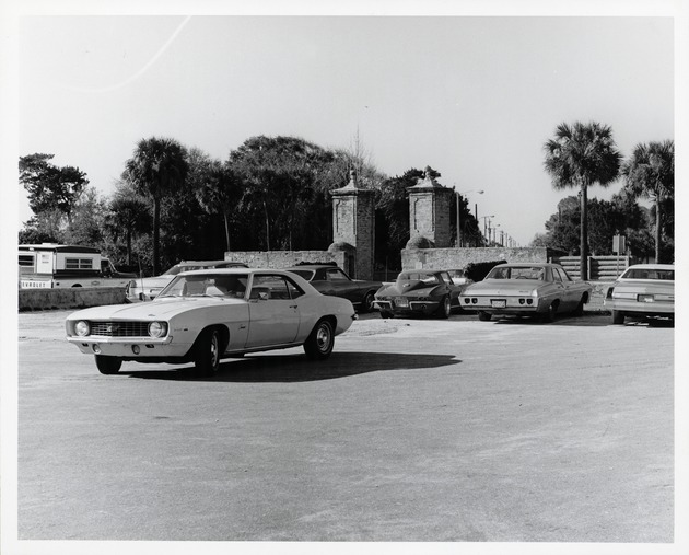 The parking lot for the Oldest Wooden School House (Genopoly House) and the City Gate in the background, looking North, ca. 1971