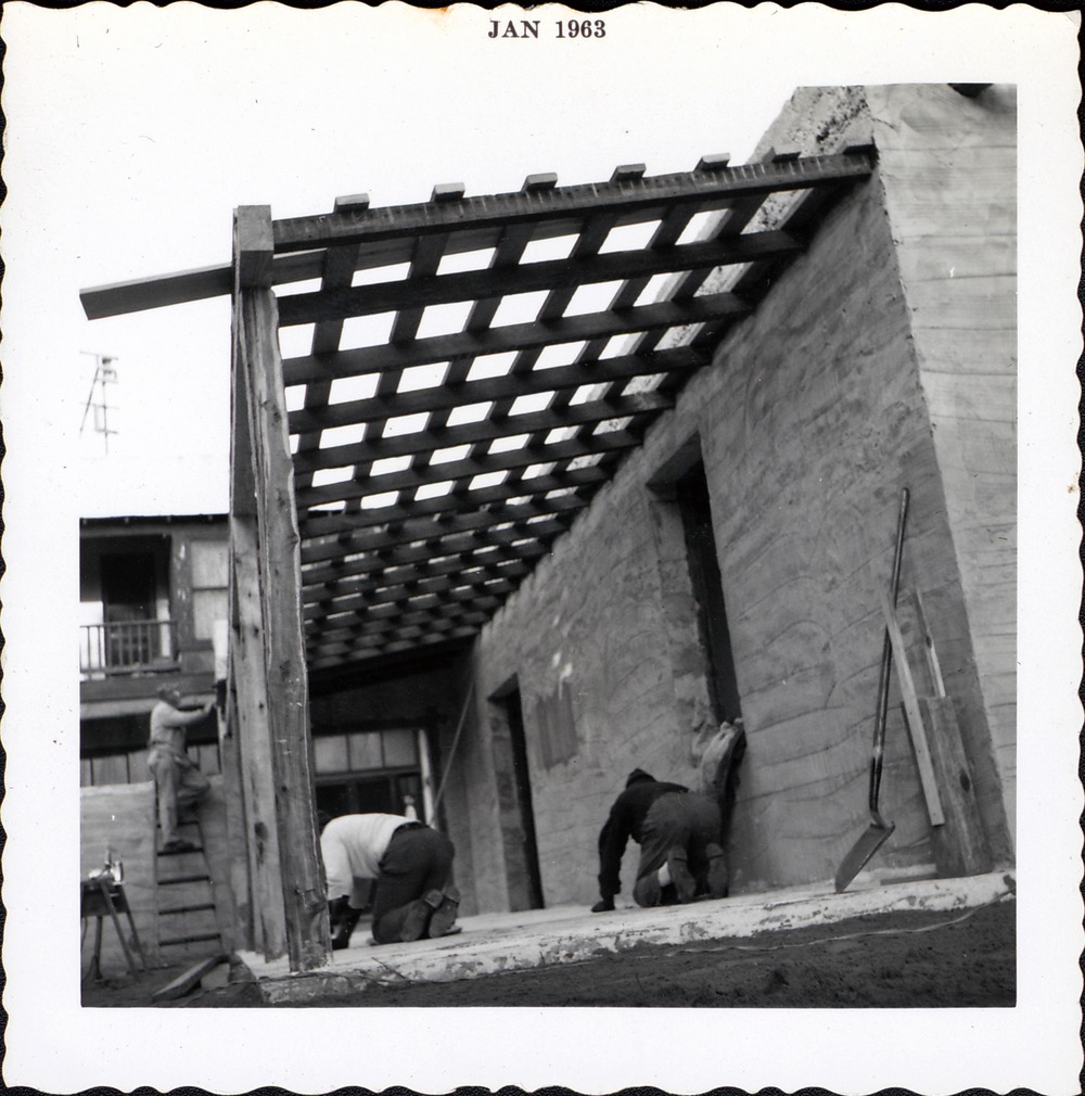 Workers finishing (grinding) the front patio of Gallegos House by hand with stones, looking West