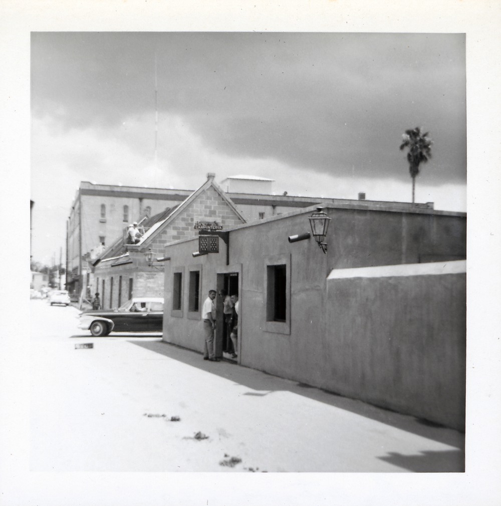 A group of man standing in the doorway of the Sanchez de Ortigosa House on St. George Street, with the restoration of the Benet House in the background, 1967