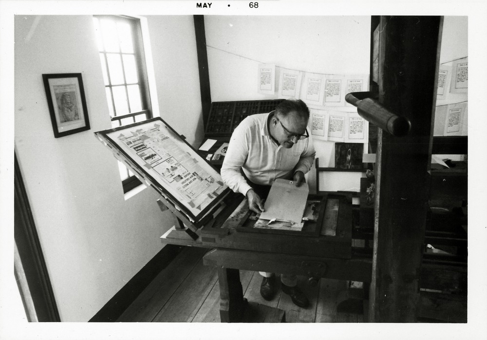 Jake Goff operating a replica printing press inside the Wells Print Shop, looking East