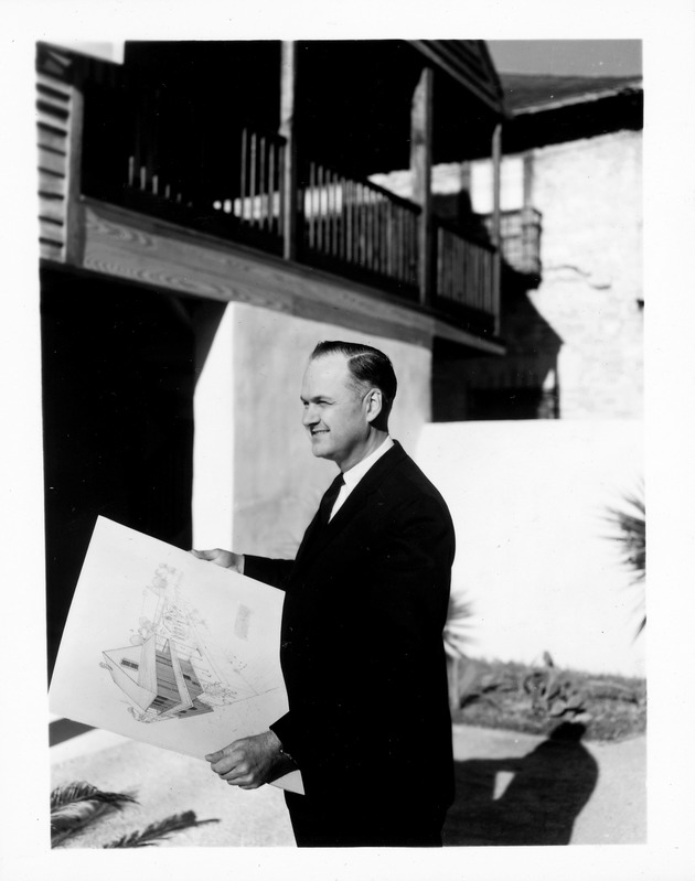 Earle Newton standing in the courtyard of the Arrivas House with an architectural rendering of the structure