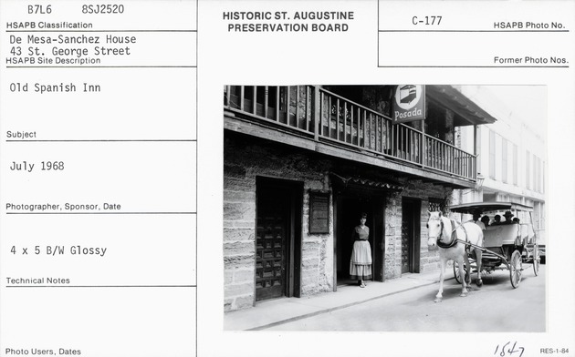 Woman standing in the doorway of the De Mesa Sanchez House with a horse-drawn carriage passing by on St. George Street
